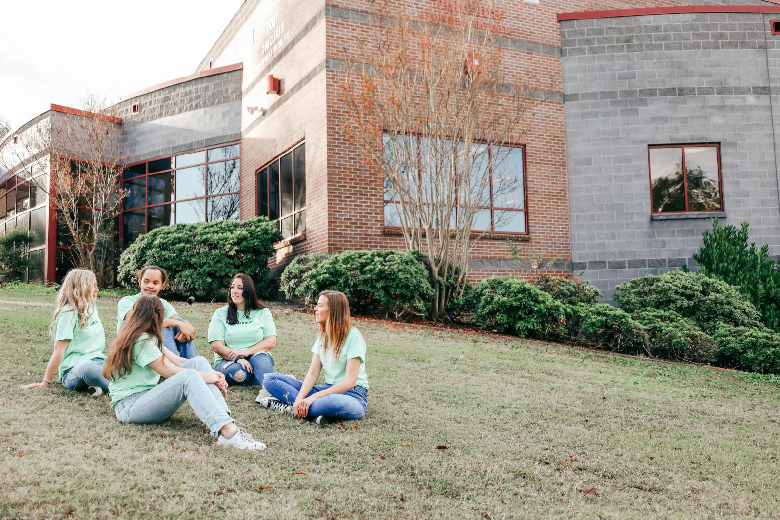 一群身穿薄荷绿买世界杯app推荐衬衫的学生坐在1300号大楼左边的草坪上聊天.